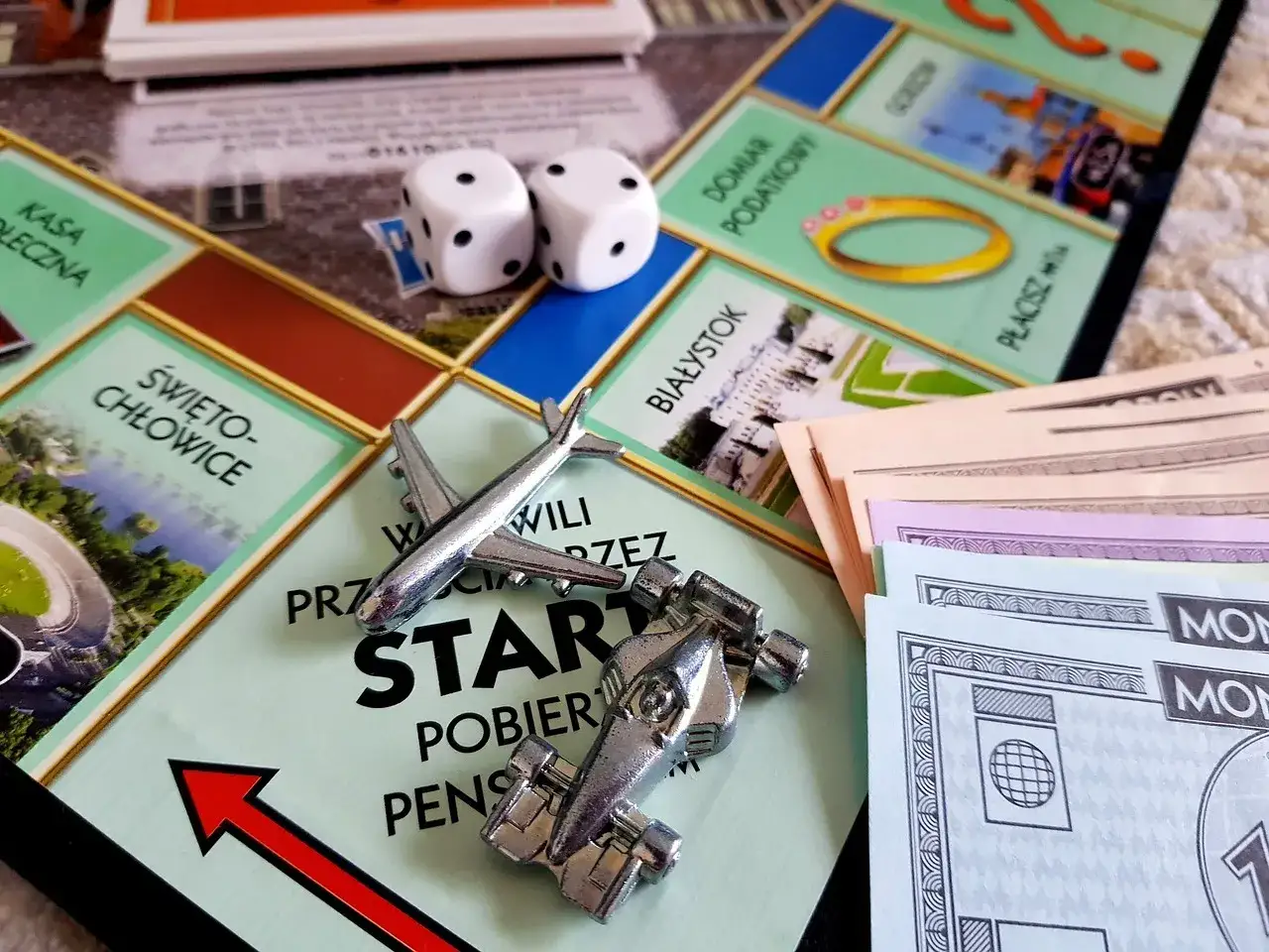 Plansza Monopoly z pionkami (samolot, bolid), kostkami i banknotami.
