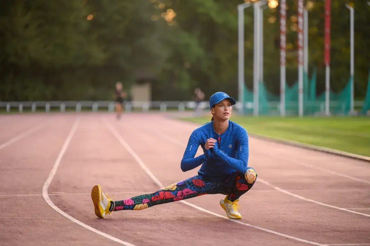 Kobieta w sportowym stroju rozciąga się na bieżni, wykonując ćwiczenie na szpagat.