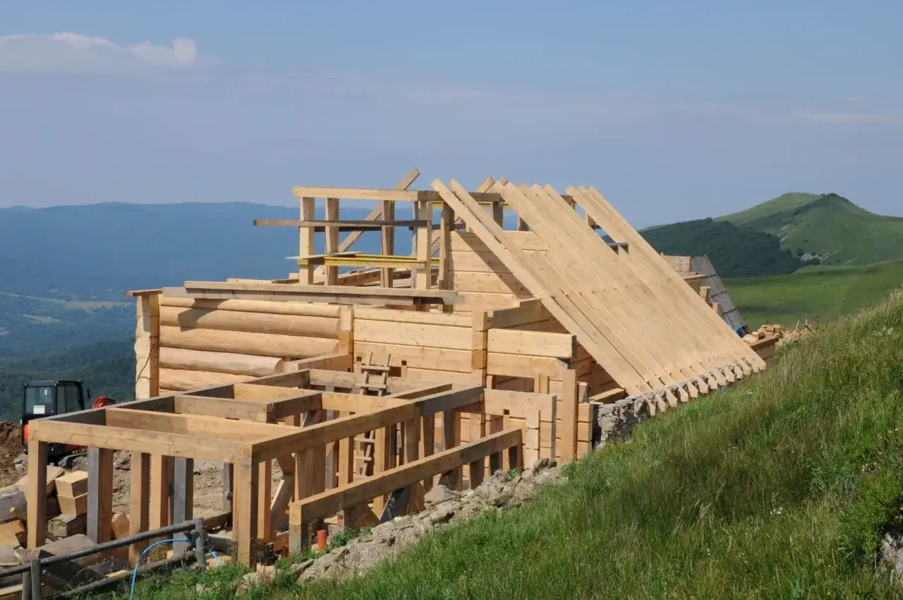 Budowa chatki Puchatka w Bieszczadach. Drewniana konstrukcja domu z bali na tle zielonych wzgórz i błękitnego nieba.