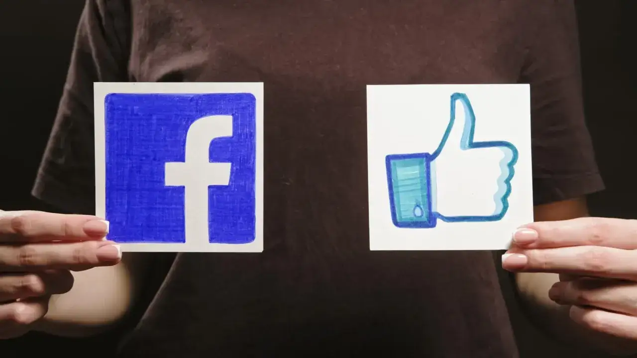 Dwie ręce trzymają kartki z logo Facebooka i kciukiem w górę.