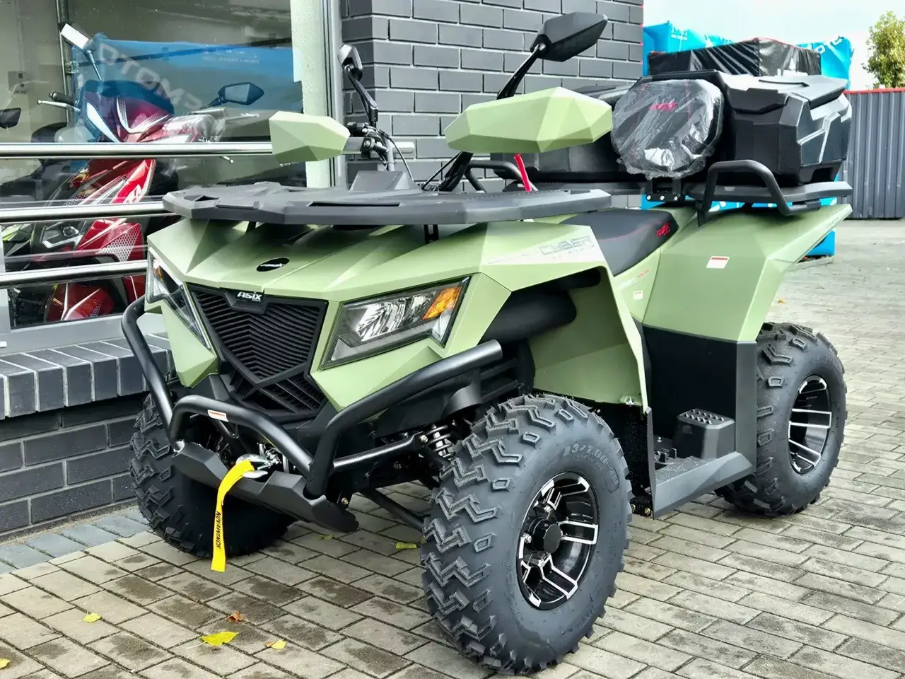 Zielony quad z bagażnikami, idealny na kategorię B. Wygląda na solidną maszynę do jazdy terenowej.