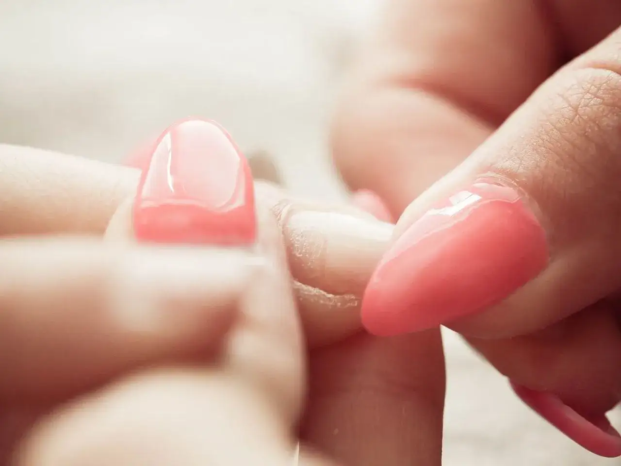 Zbliżenie na dłonie, gdzie widać proces usuwania manicure tytanowego. Różowe paznokcie są w trakcie zdejmowania.