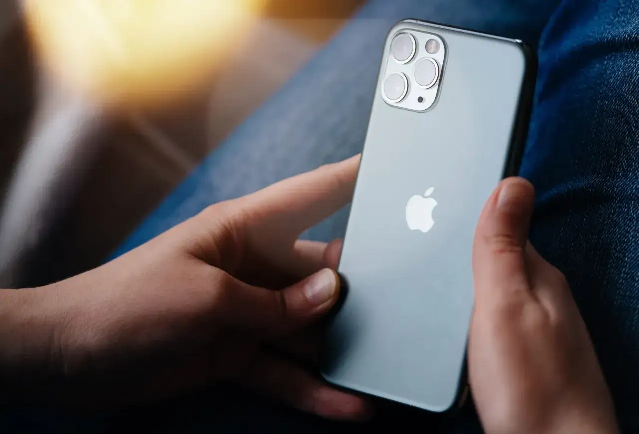 Dłonie trzymające szare iPhone'a z widocznym logo Apple i modułem aparatów.