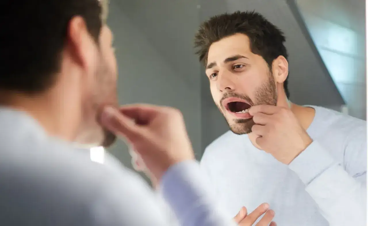 Mężczyzna w lustrze sprawdza, czy nie ma krwiaka na języku po uderzeniu.