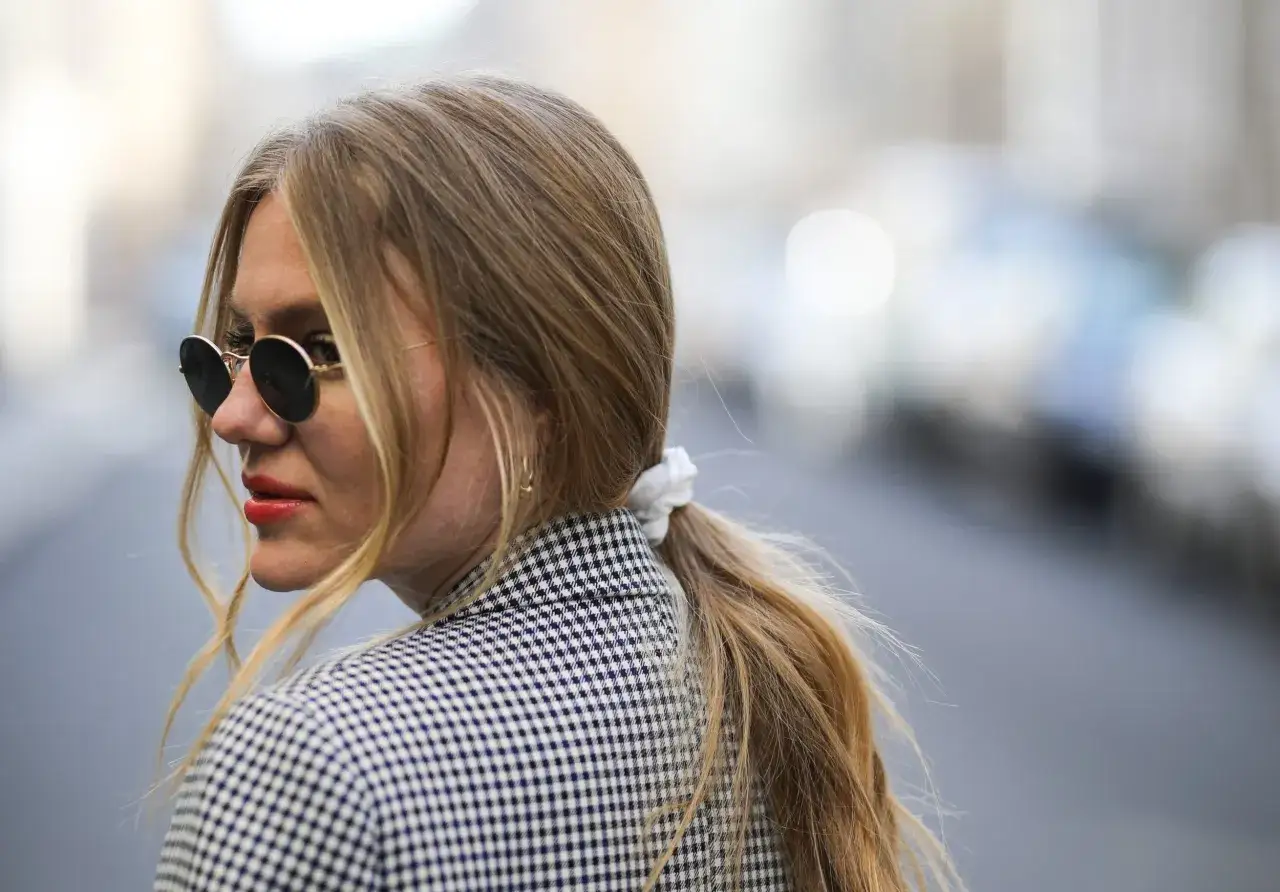 Kobieta w okularach przeciwsłonecznych i marynarce w kratkę, z blond kucykiem.