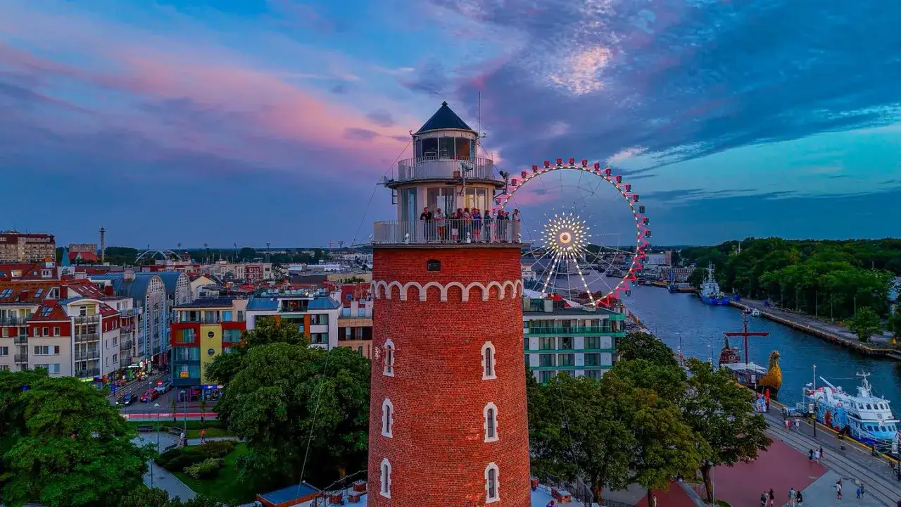 Widok na latarnię morską, diabelski młyn i port w Kołobrzegu o zachodzie słońca.