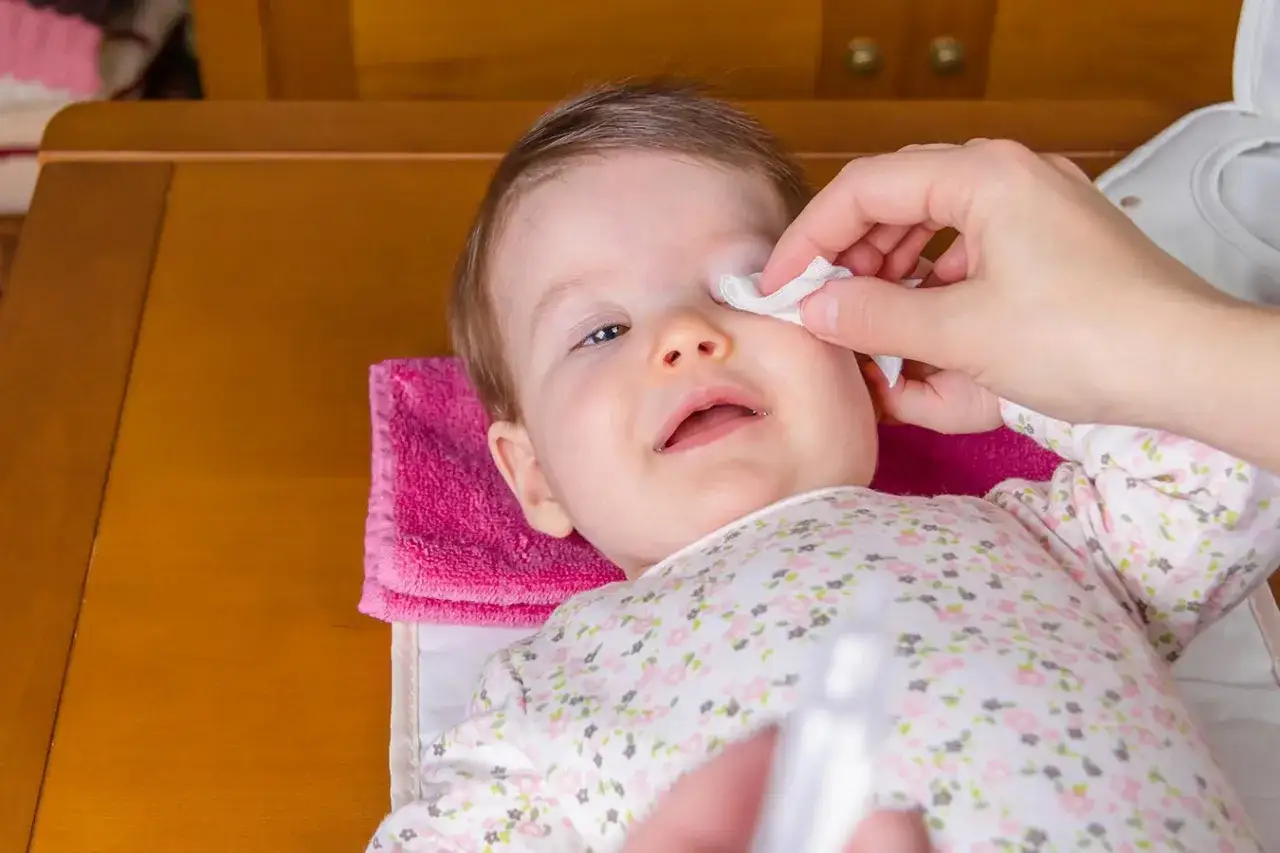 Delikatne przemywanie oczu niemowlaka wacikiem nasączonym solą fizjologiczną do oczu.