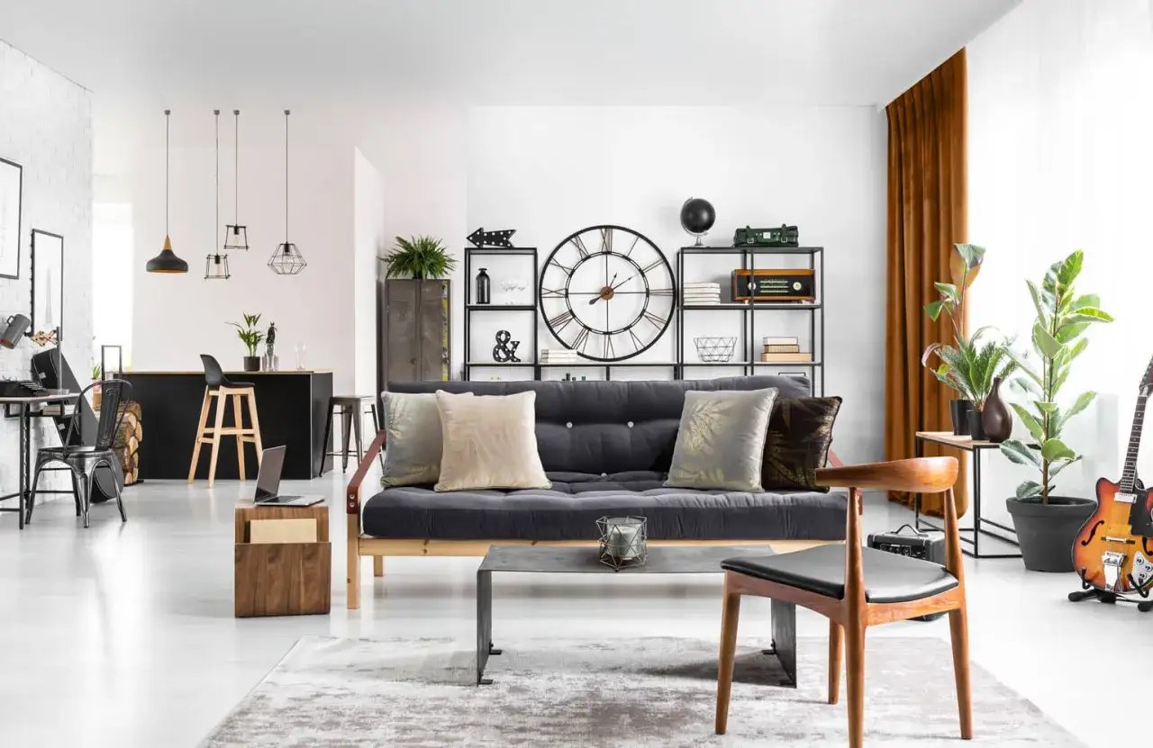 Jak rozjaśnić salon z ciemnymi meblami? Jasne ściany, duży dywan i złote akcenty na poduszkach dodają lekkości.