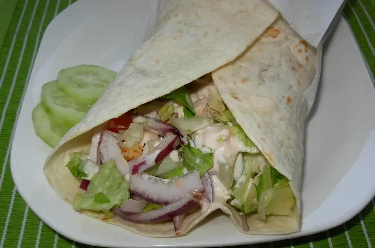 Pyszny domowy kebab w tortilli z kurczakiem, warzywami i sosem. Obok plastry ogórka.