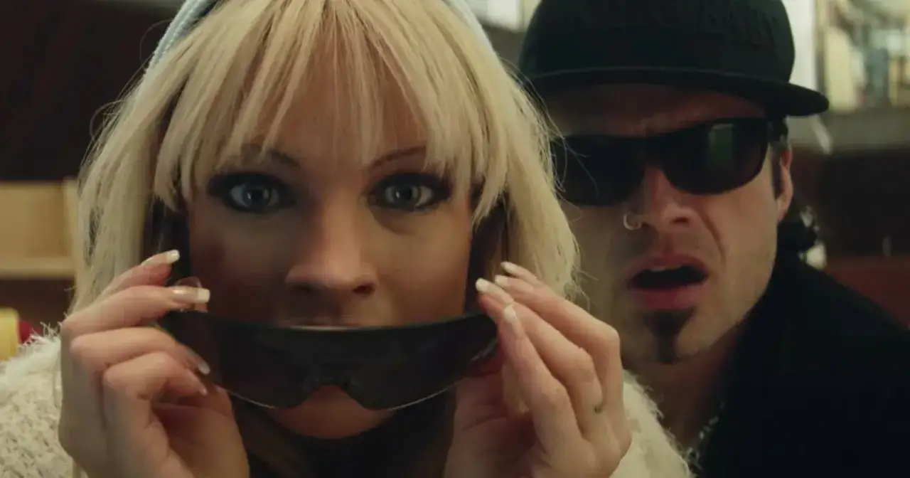 Pam i Tommy w okularach przeciwsłonecznych, ona trzyma je przed ustami, on patrzy z zaskoczeniem.