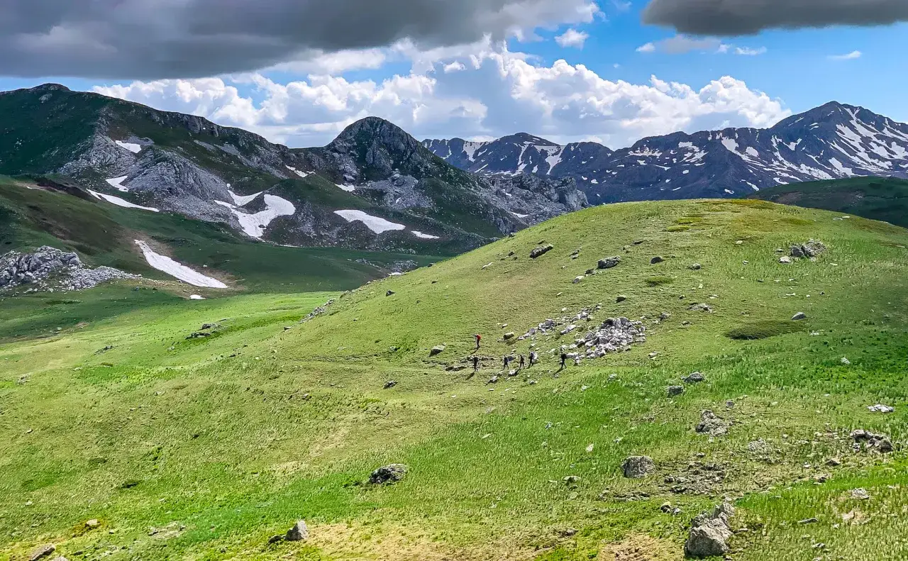 Grupa turystów wędruje po zielonych zboczach gór Macedonii, podziwiając skaliste szczyty i resztki śniegu.