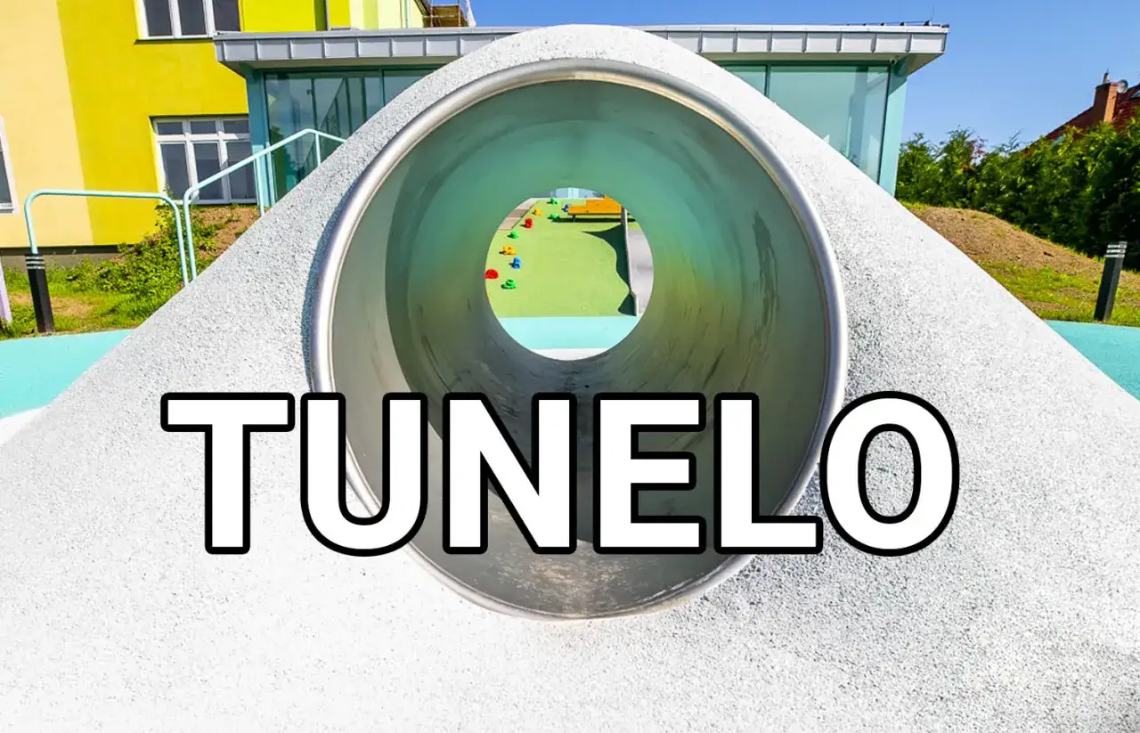 Tunel na placu zabaw z widokiem na kolorowe elementy i budynek.