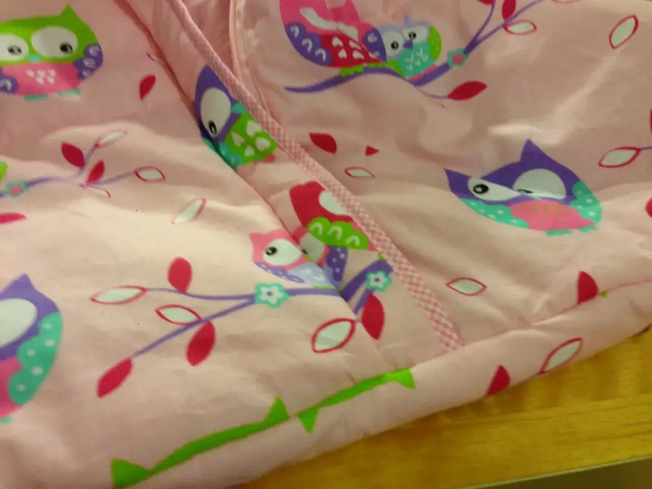 Różowy śpiworek niemowlęcy z kolorowym wzorem sów na gałęziach.