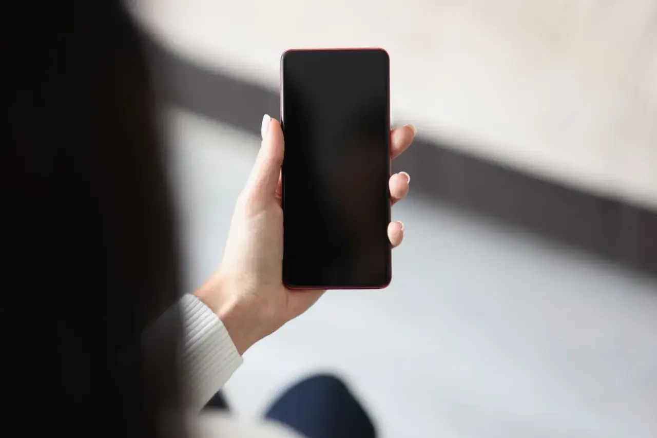 Dłoń trzyma telefon z czarnym ekranem, być może z powodu pogorszenia jakości zdjęć w telefonie.