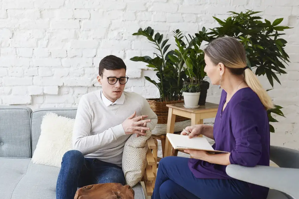 Mężczyzna w okularach rozmawia z kobietą, która notuje. To typowa scena, gdy psychoterapeuta pomaga pacjentowi.