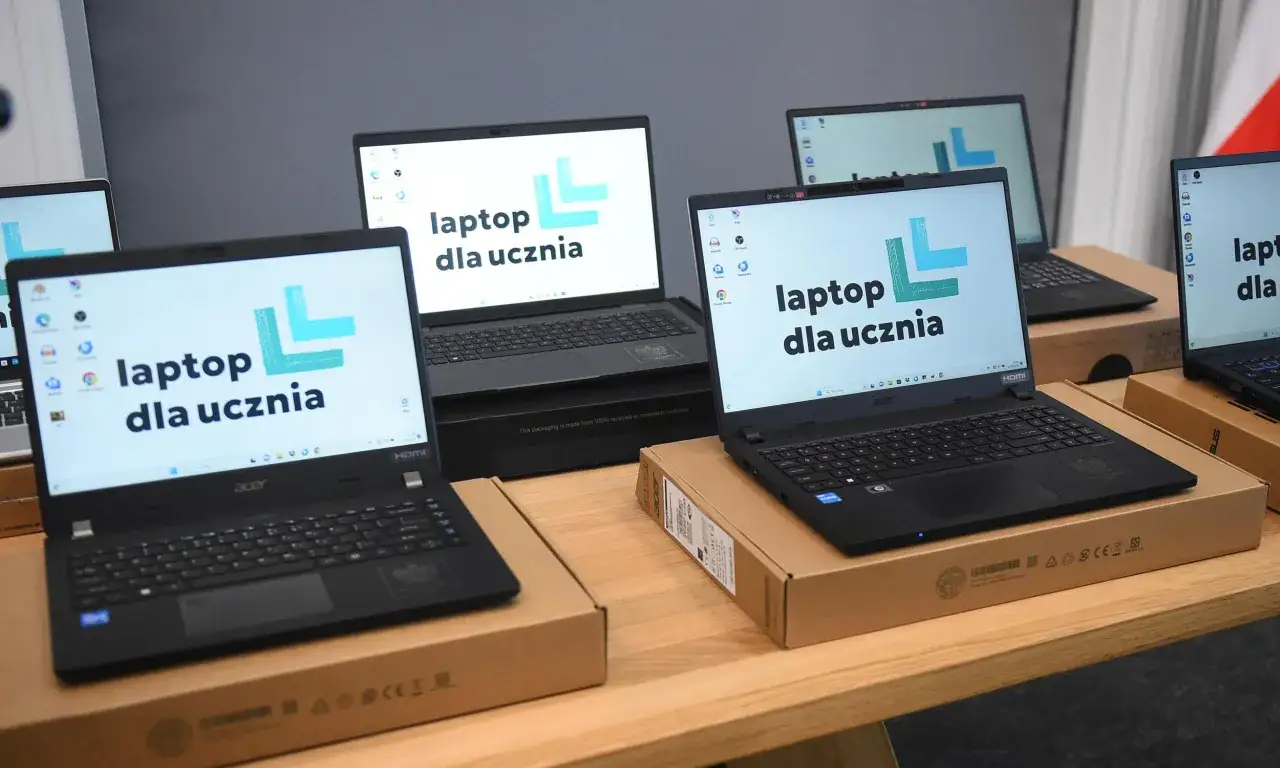Kilka laptopów z logo "laptop dla ucznia" na ekranach, gotowych do przekazania uczniom.