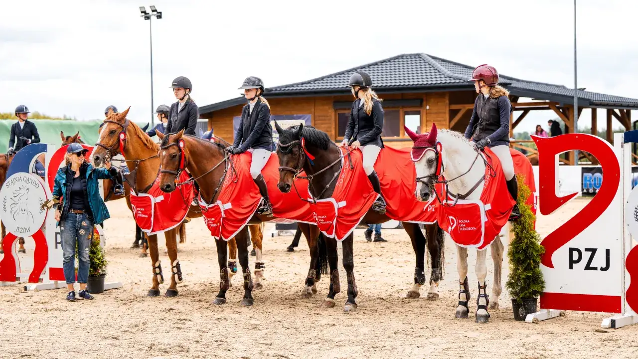 Jeźdźcy i konie w czerwonych derkach z logo "Polska Liga Jeździecka" na zawodach. Sukcesy klubu jeździeckiego Preria Wilkowice.