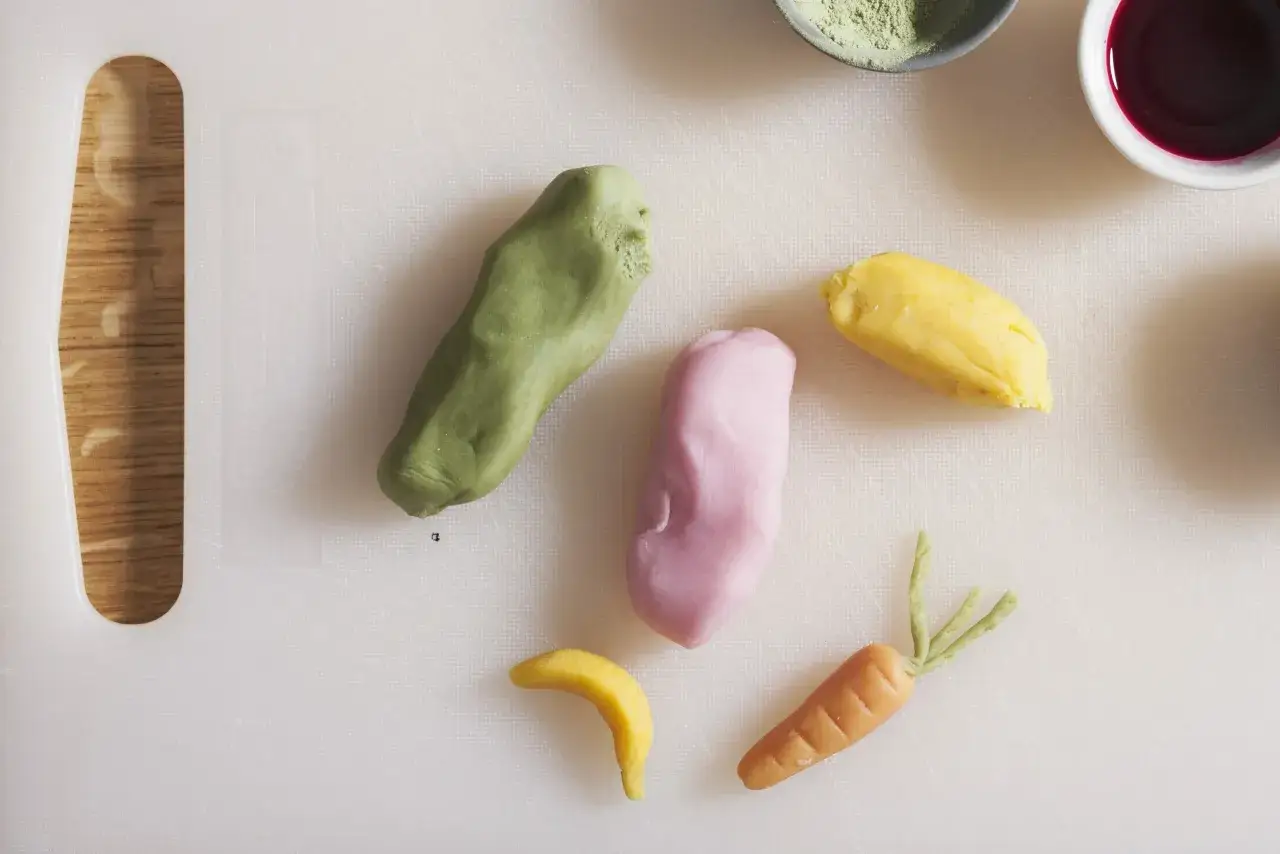 Kolorowe masy cukrowe uformowane w marchewkę, banana i inne kształty na białej desce.