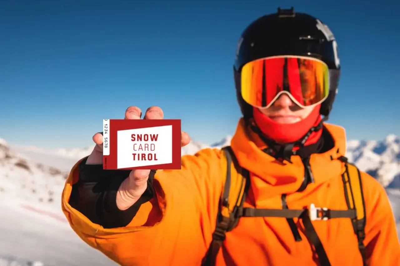 Narciarz w kasku i goglach pokazuje kartę "Snow Card Tirol". To jest skipass, który umożliwia dostęp do wyciągów.