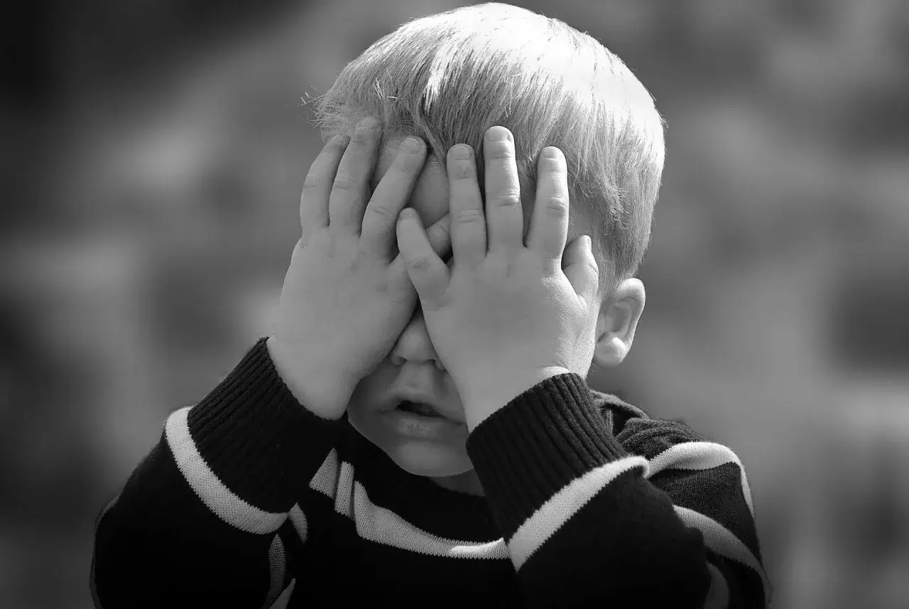 Chłopiec zakrywa twarz dłońmi, co może być oznaką dziwnego zachowania 10-latka, gdy próbuje ukryć emocje.