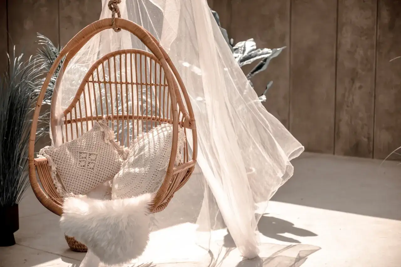 Rattanowy fotel wiszący z poduszkami, zawieszony na linie. Dowiedz się, jak zamontować fotel wiszący do sufitu, by stworzyć przytulny kącik.