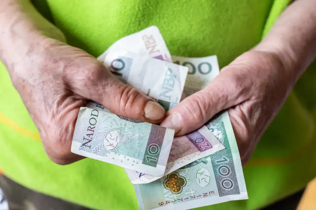 Dłonie starszej osoby trzymają polskie banknoty: 10, 20 i 100 zł.