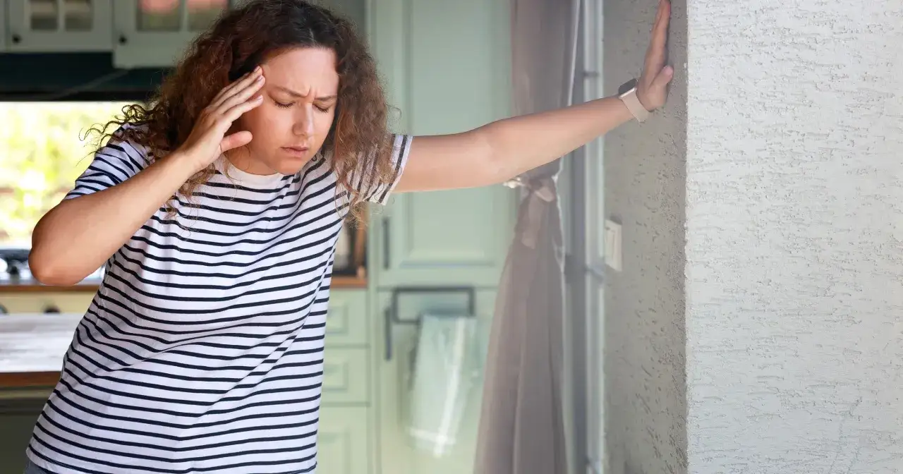 Kobieta w paski trzyma się za głowę, opierając się o ścianę.