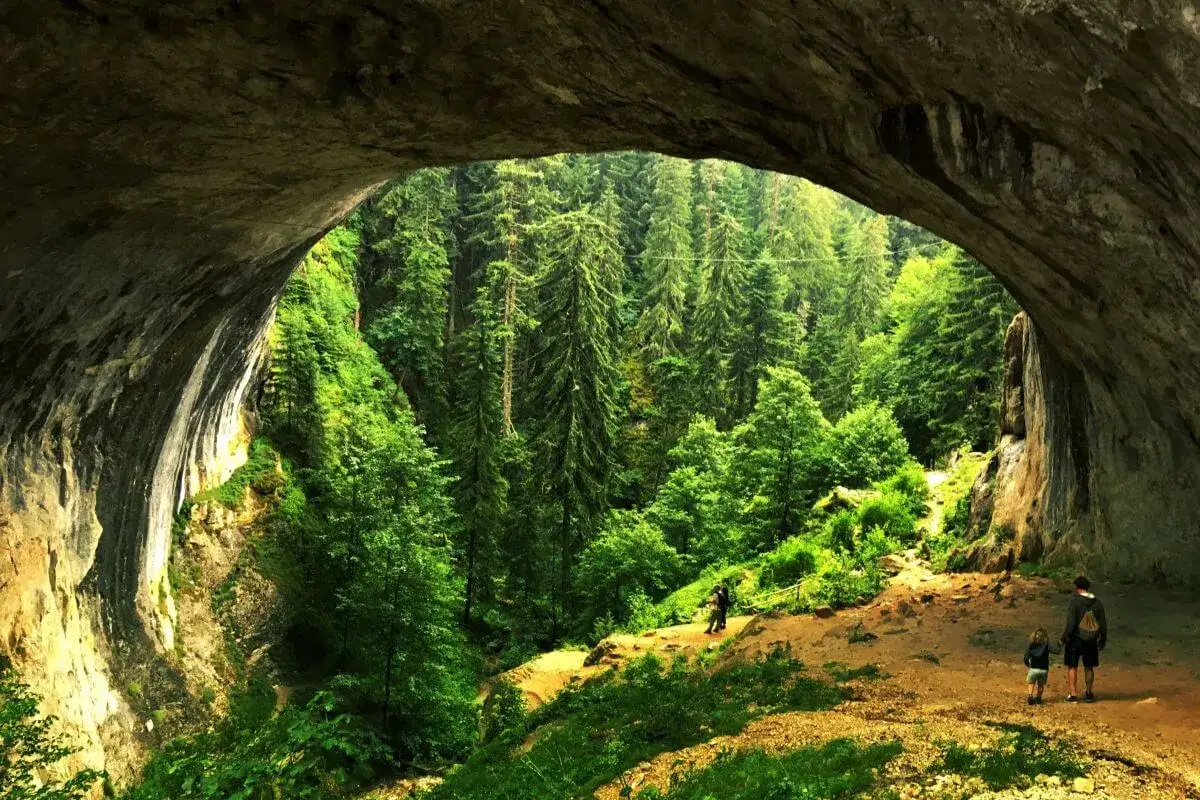 Wspaniałe skalne okno w górach Rodopy otwiera widok na bujny, zielony las. Ludzie spacerują ścieżką.