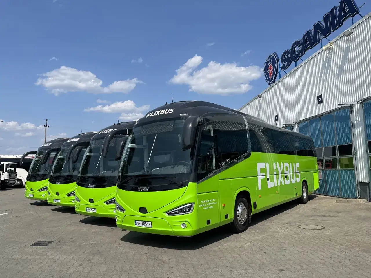 Rząd zielonych autobusów Flixbus zaparkowanych przed budynkiem z logo Scania.