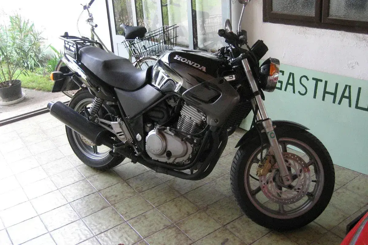 Czarny motocykl Honda z widocznym silnikiem i wydechem, gotowy do jazdy. Obok stoi rower.