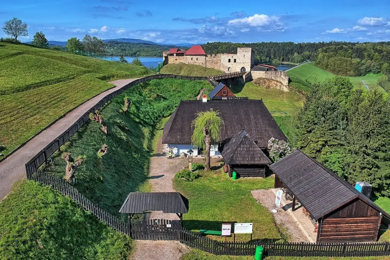 Widok z lotu ptaka na skansen z zamkiem, jeziorem i zielonymi wzgórzami.