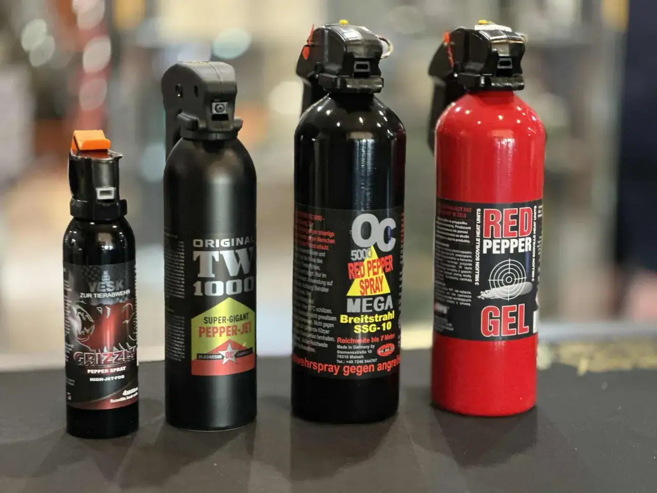 Cztery różne pojemniki z gazem pieprzowym, w tym jeden czerwony z napisem "RED PEPPER GEL".