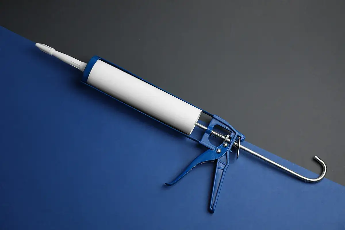 Niebieski pistolet do silikonu z białą tubą na tle dwóch kolorów.