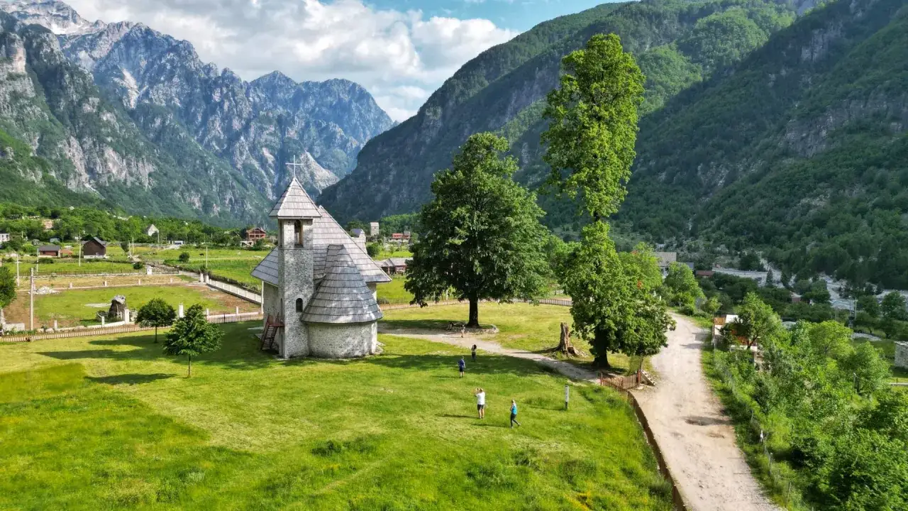 Kamienna cerkiew w Theth, Albania, otoczona zielonymi wzgórzami i majestatycznymi górami.
