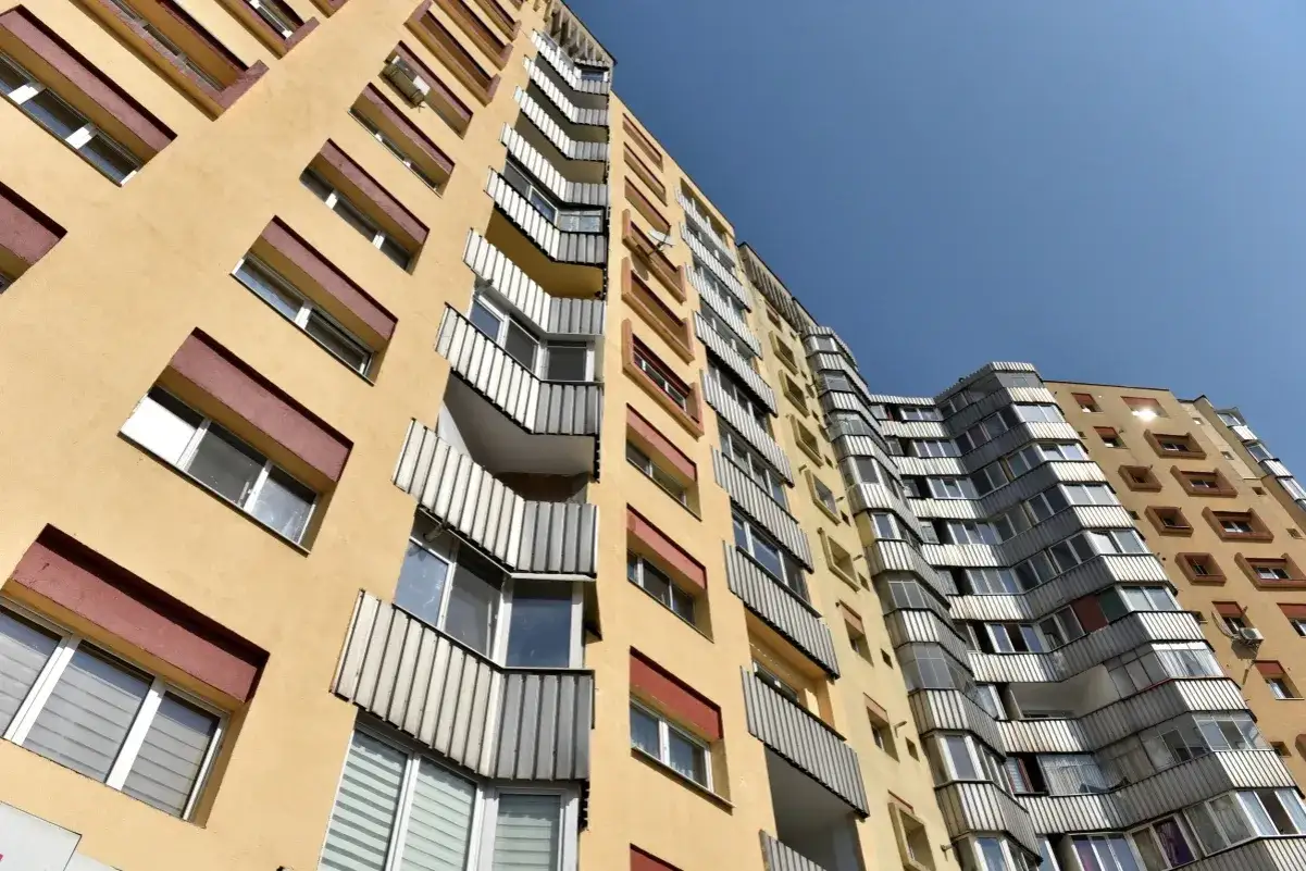 Wysoki, żółty blok mieszkalny z balkonami. Szukasz informacji, jak wypełnić wniosek o mieszkanie komunalne wzór?