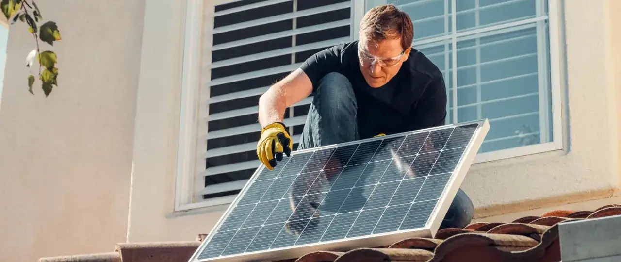 Mężczyzna w okularach ochronnych montuje panel słoneczny na dachu, walcząc ze zmianami klimatycznymi.