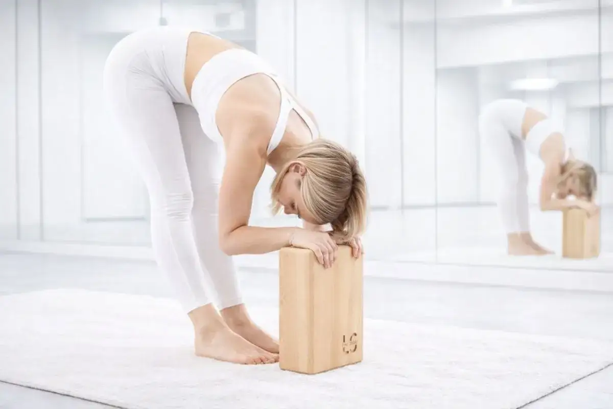Kobieta w białym stroju do jogi pokazuje, jak używać kostki do jogi do pogłębienia skłonu.