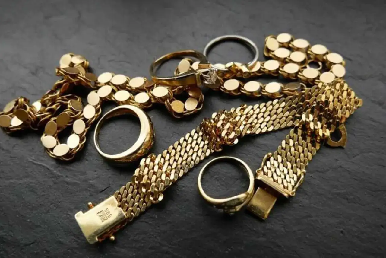 Złota biżuteria: naszyjnik, bransoletki i pierścionki na ciemnym tle.