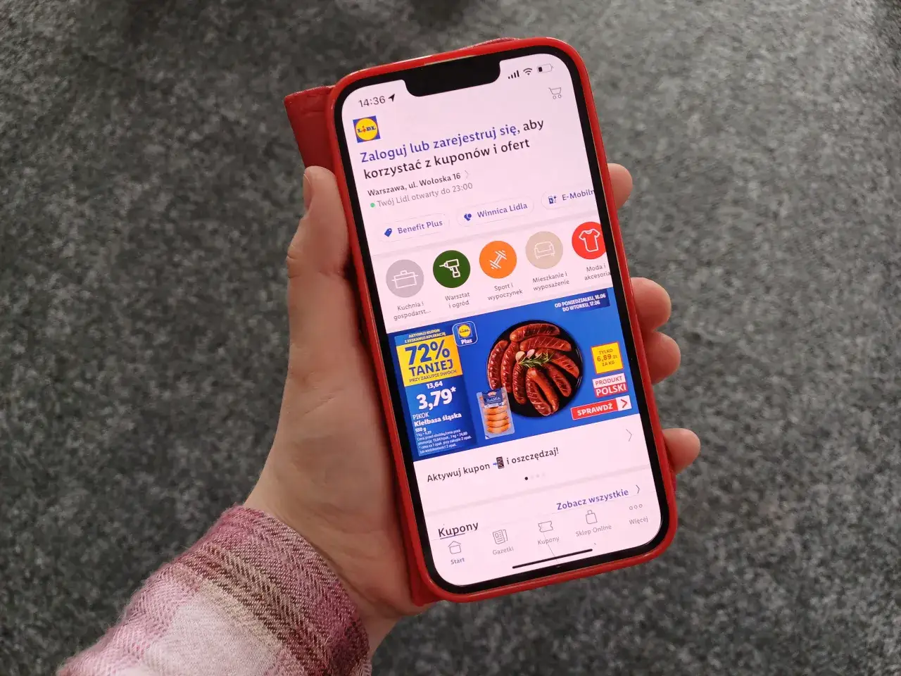Dłoń trzymająca smartfon z aplikacją Lidl Plus, na ekranie widoczna promocja na kiełbasę.