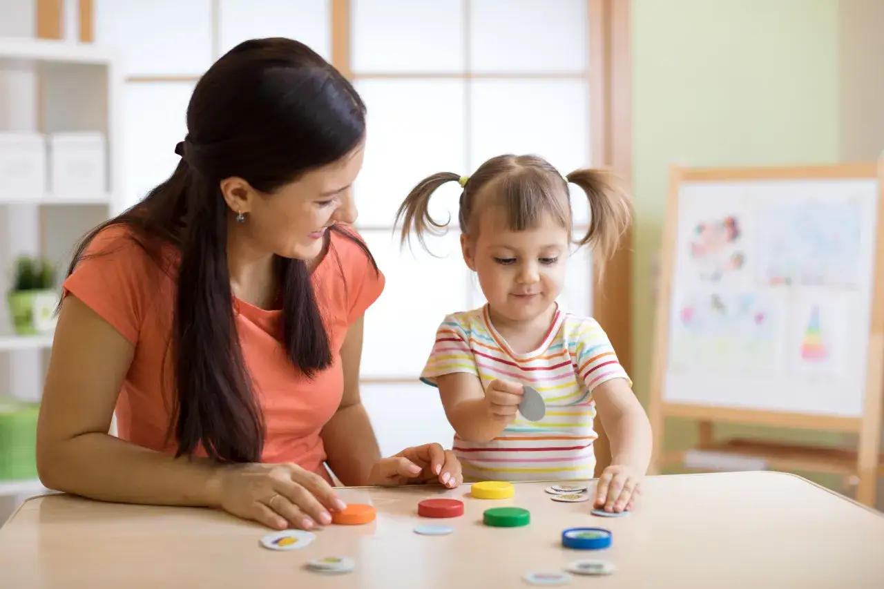 Opiekunka dziecięca z uśmiechem bawi się z dzieckiem, układając kolorowe kółka. To praca, która daje radość, ale warto wiedzieć, ile zarabia opiekunka dziecięca.