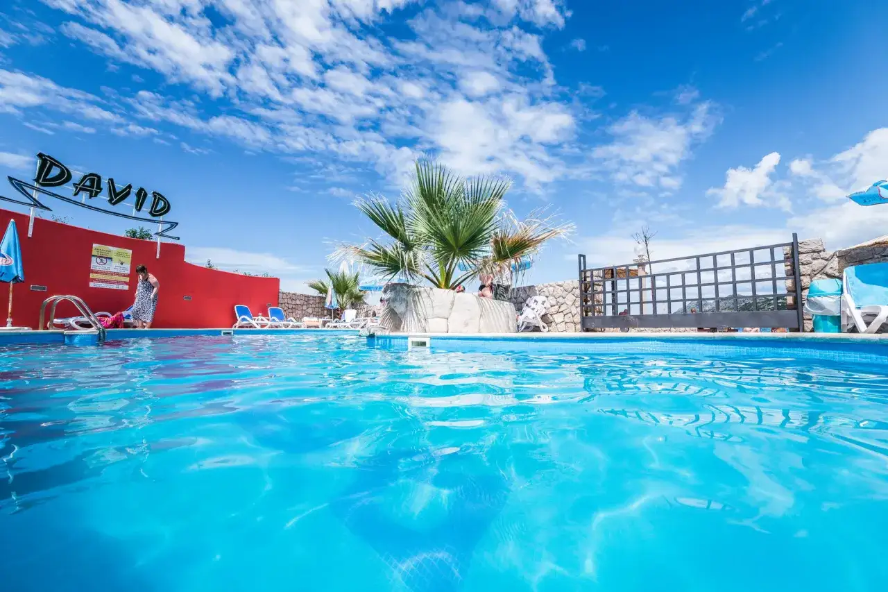 Basen z turkusową wodą, palmy i czerwony budynek z napisem "DAVID". Idealne miejsce na czarnogóra bez pośpiechu.