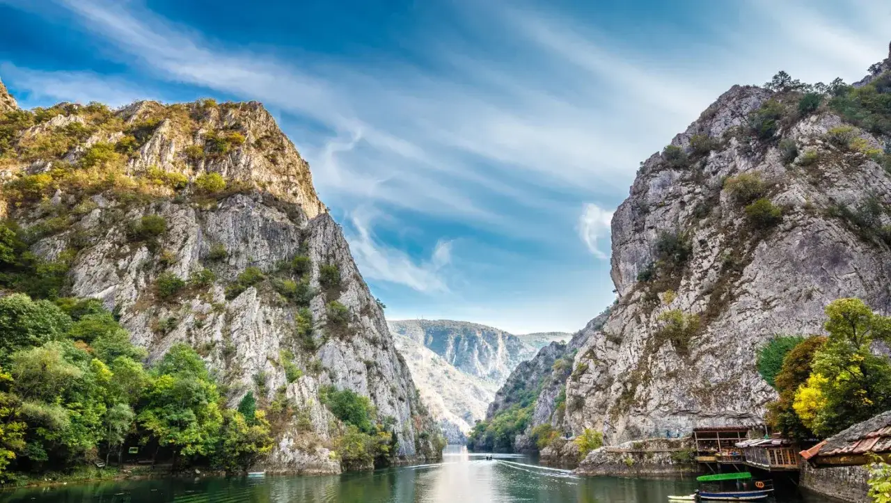 Majestatyczny kanion Matka, gdzie rzeka przecina skalne ściany, a łodzie suną po spokojnej wodzie pod błękitnym niebem.