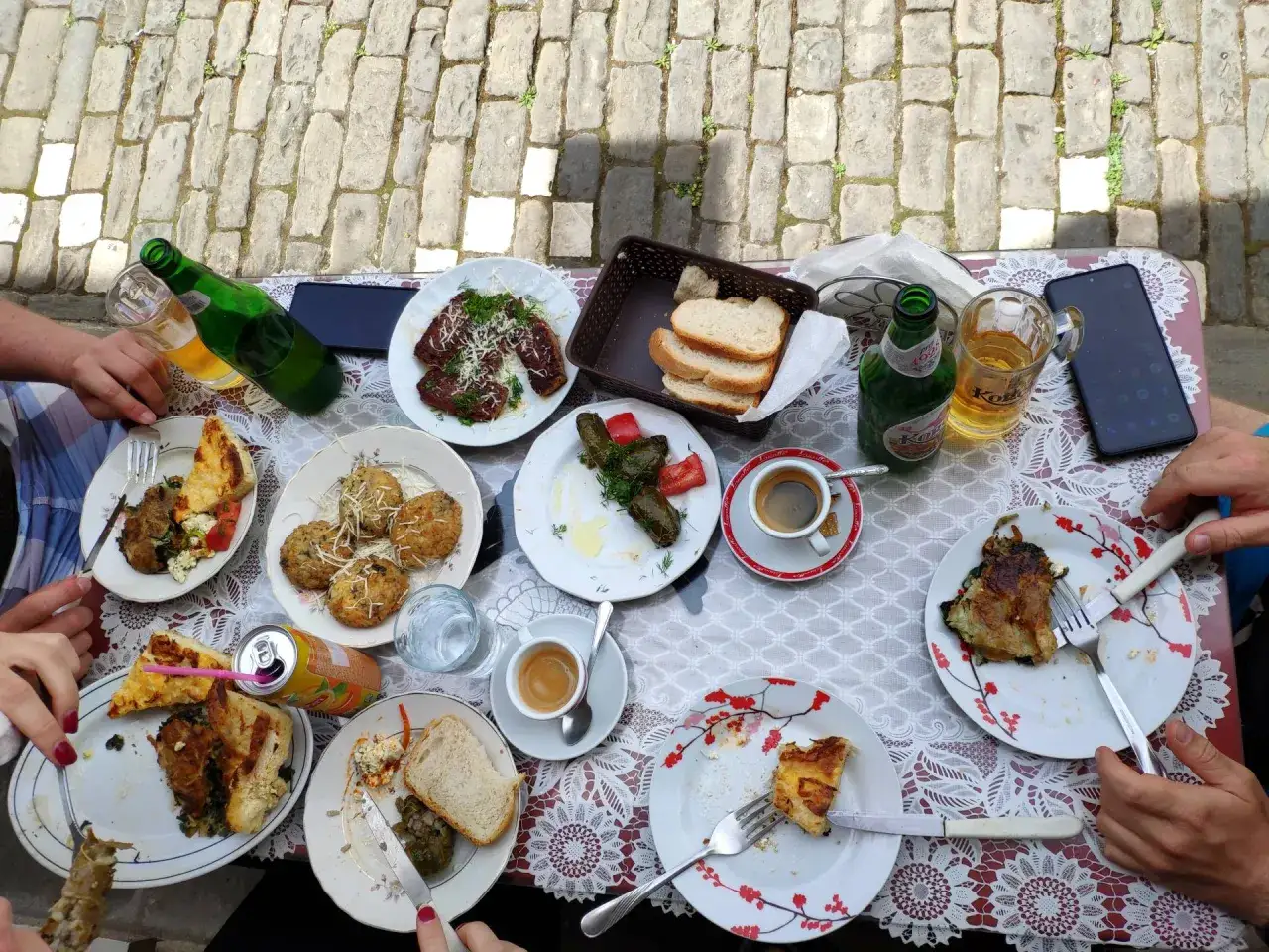 Stół zastawiony pysznym jedzeniem, typowym dla Albanii. Widać dania mięsne, gołąbki, pieczywo, kawę i piwo.