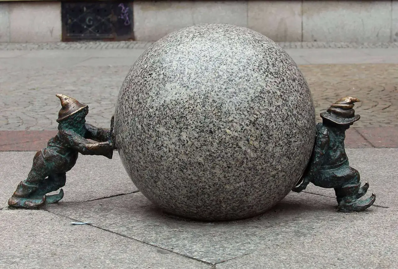 Dwa wrocławskie krasnale pchają kamienną kulę. Ile jest krasnali we Wrocławiu? Tyle, ile potrzeba do wspólnego celu!