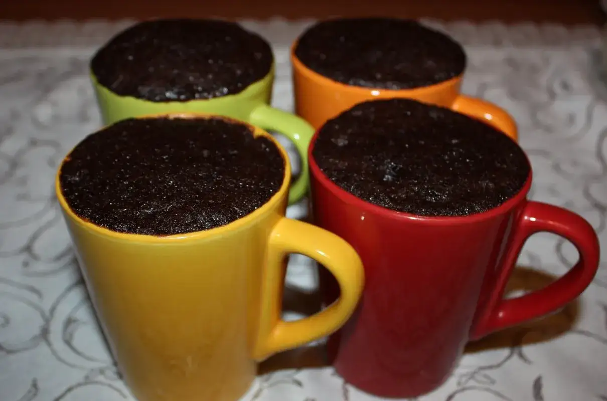 Cztery kolorowe kubki: żółty, zielony, pomarańczowy i czerwony, wypełnione po brzegi pysznym, ciemnym ciastem.