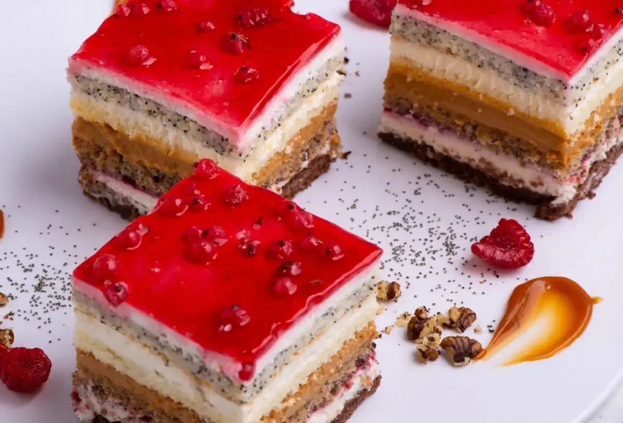 Kawałki wielowarstwowego ciasta z galaretką z czerwonych porzeczek, makiem i kremem.