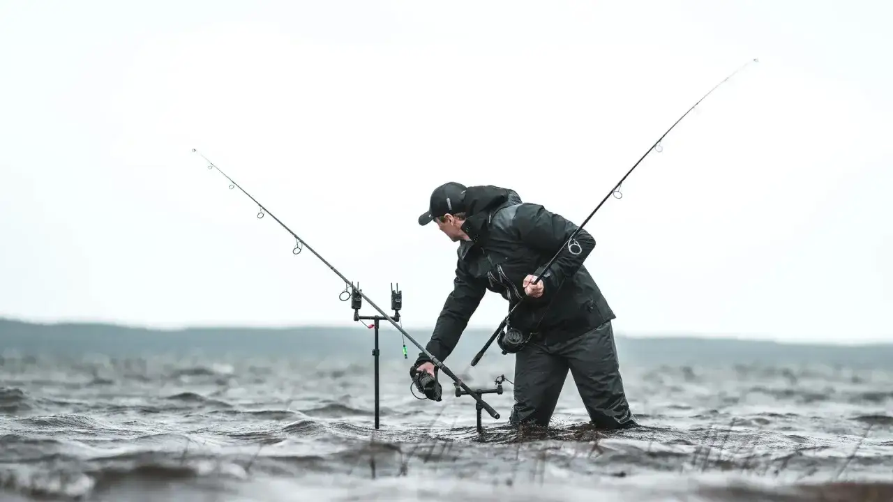 Wędkarz w wodzie z kilkoma wędkami. Zastanawia się, ile wędek na kartę wędkarską można zabrać.