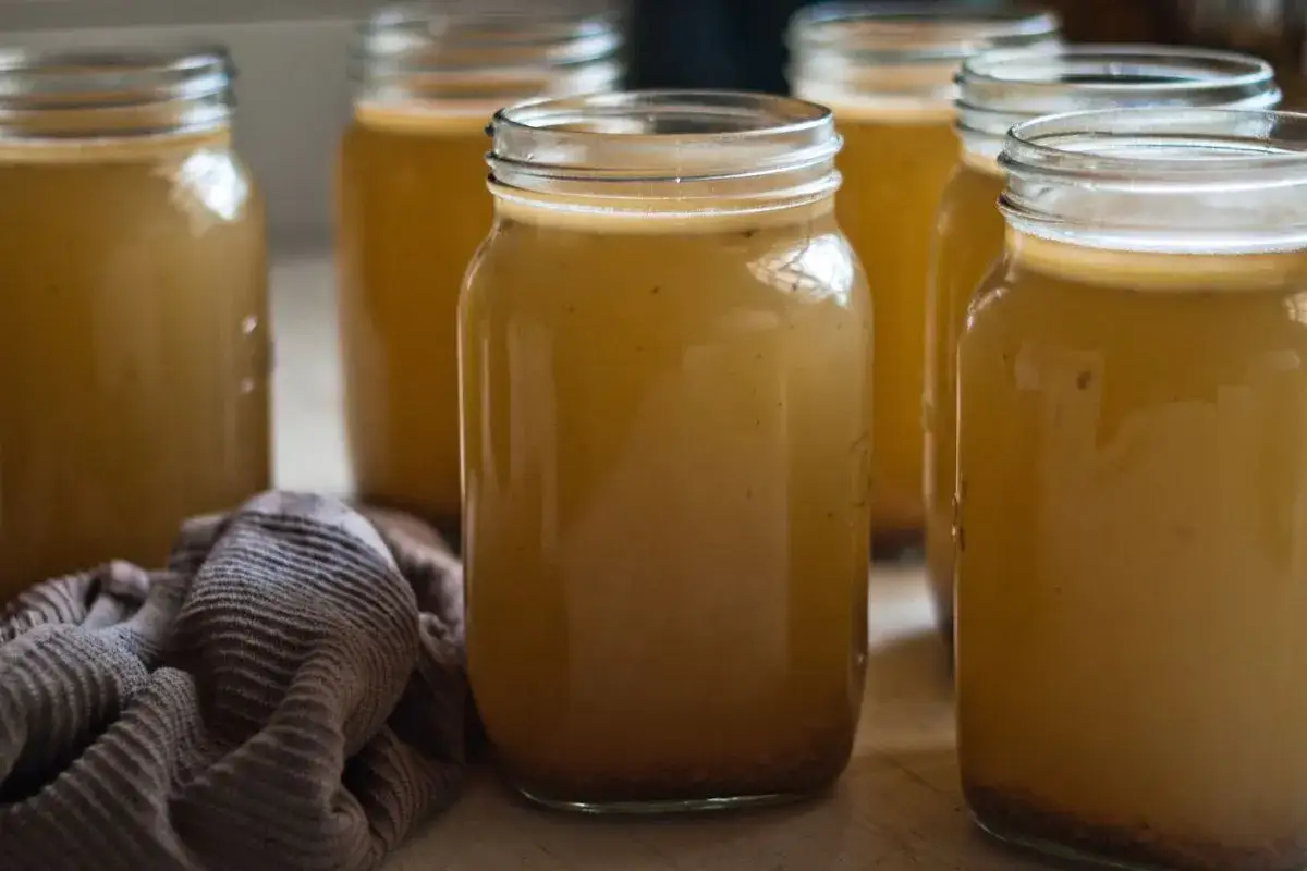 Kilka słoików z bulionem lub zupą na drewnianym blacie.