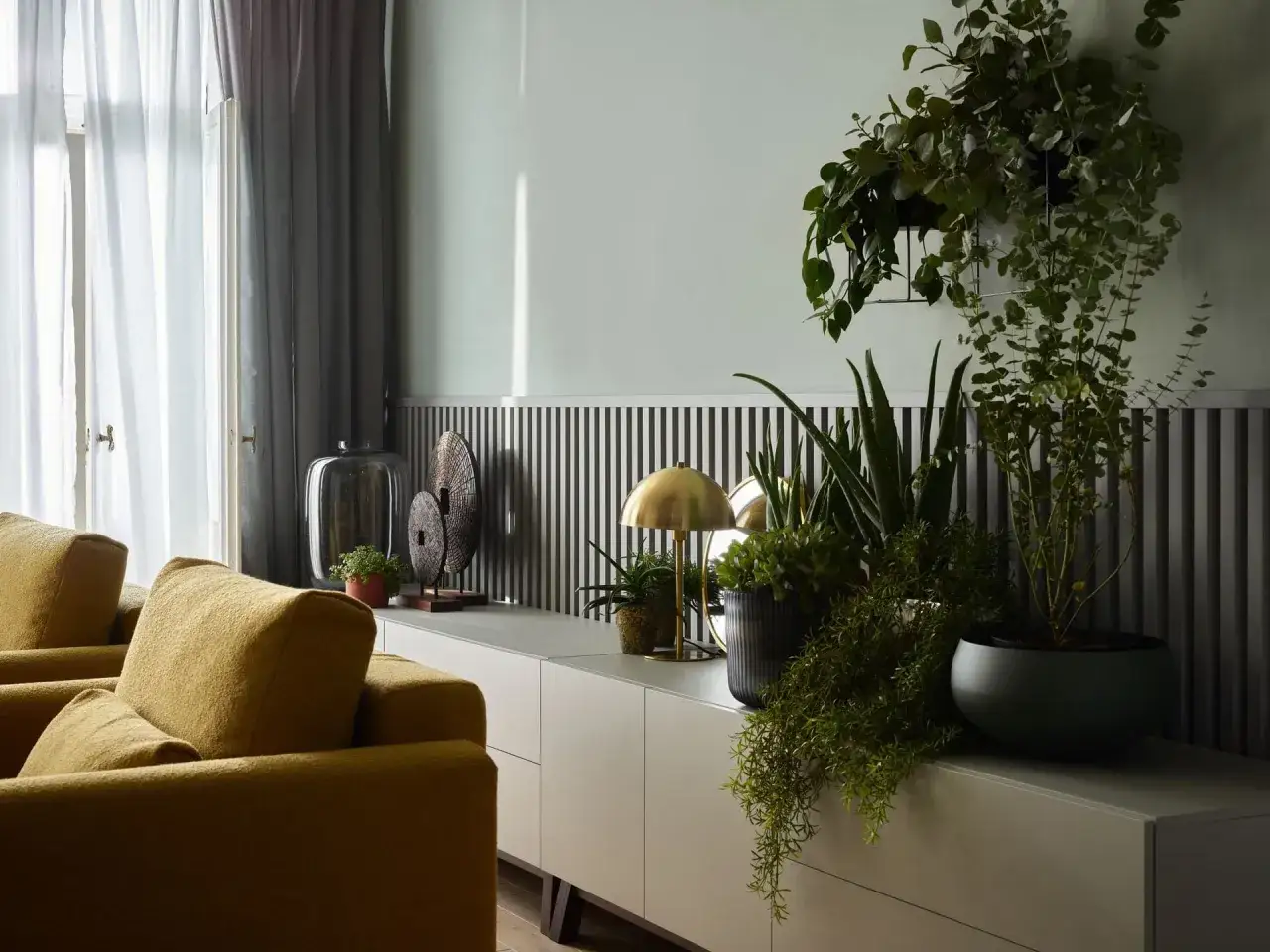 Szare ściany z czym łączyć? Z żółtymi meblami i mnóstwem zieleni. Wnętrze z nowoczesną komodą, lampką i roślinami.