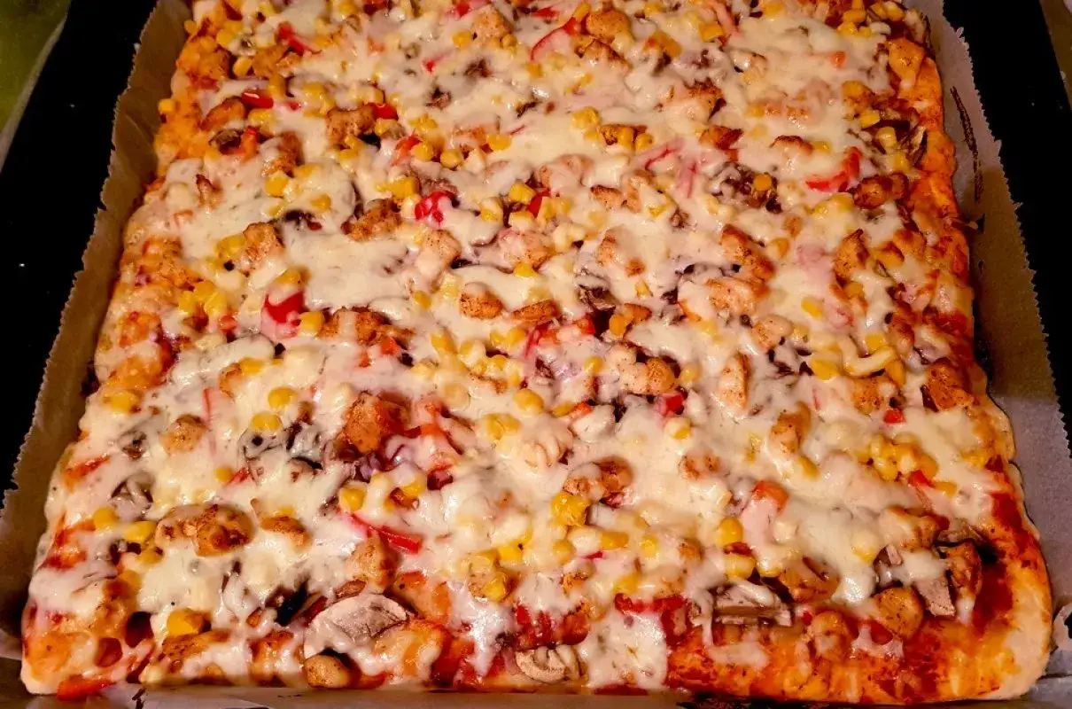 Prostokątna pizza z kurczakiem, kukurydzą, papryką i serem.